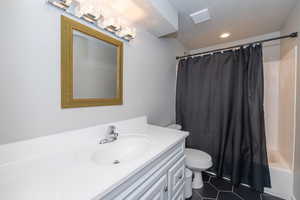 Bathroom with vanity, shower / tub combo with curtain, and dark tile patterned flooring