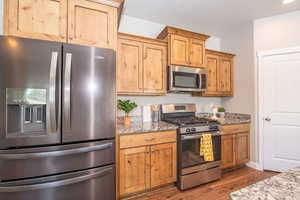 Kitchen featuring stainless steel appliances, light stone counters, and dark wood-type flooring