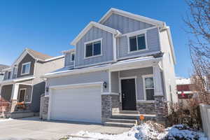 Craftsman-style home featuring board and batten siding, a garage, stone siding, driveway, and covered porch