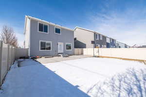 Snow covered house featuring a fenced backyard, stucco siding, and a patio