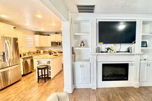 Kitchen featuring stainless steel appliances, a textured ceiling, a kitchen bar, light wood-style floors, and light stone countertops