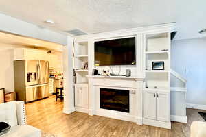 Living area featuring light wood-style floors, a textured ceiling, and a glass covered fireplace