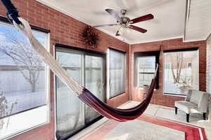 Sunroom featuring brick wall, healthy amount of natural light, and crown molding