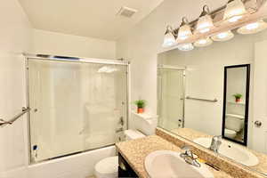 Full bath featuring vanity, bath / shower combo with glass door, and a textured ceiling