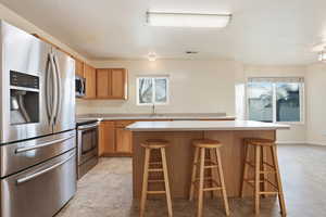 Kitchen featuring stainless steel appliances, light countertops, a kitchen bar, a center island, and wood finish cabinets