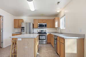 Kitchen featuring a kitchen island, stainless steel appliances, light countertops, a breakfast bar, and wood finish cabinets