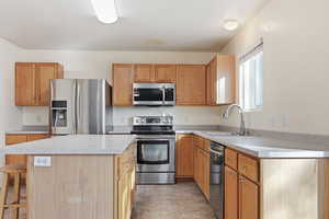 Kitchen with a center island, stainless steel appliances, light countertops, a breakfast bar area, and stone finish vinyl flooring