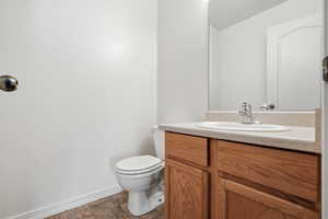 Half bath with vanity, a textured wall, and dark stone finish flooring