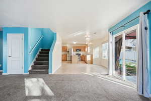 Unfurnished living room featuring stairway and light colored carpet