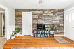 Living room with wooden walls, hardwood / wood-style flooring, ceiling fan, an accent wall, and a wainscoted wall