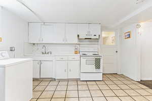 Kitchen featuring washer / dryer, white range with electric stovetop, light countertops, white cabinets, and backsplash