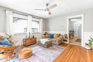 Living room featuring hardwood / wood-style flooring, a wainscoted wall, a ceiling fan, and a textured ceiling