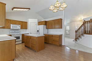 Kitchen featuring a chandelier, white appliances, wood finish cabinets, light countertops, and vaulted ceiling