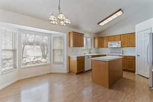 Kitchen featuring a kitchen island, vaulted ceiling, light countertops, hanging lights, and white appliances