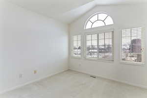 Unfurnished room with vaulted ceiling and light colored carpet