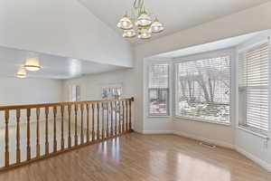 Empty room featuring a chandelier, light wood-type flooring, and vaulted ceiling