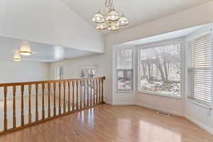 Spare room featuring light wood-style floors, a chandelier, and lofted ceiling