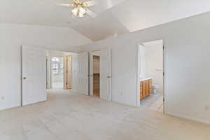 Unfurnished bedroom with ensuite bathroom, a spacious closet, light colored carpet, lofted ceiling, and a ceiling fan