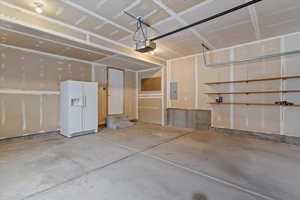 Garage featuring white refrigerator with ice dispenser, electric panel, and a garage door opener