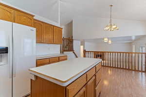 Kitchen with white fridge with ice dispenser, light countertops, wood finish cabinets, light wood-type flooring, and a kitchen island