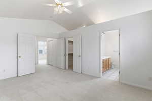 Unfurnished bedroom featuring ensuite bath, light colored carpet, a spacious closet, lofted ceiling, and a ceiling fan