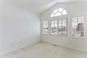 Carpeted empty room with vaulted ceiling and baseboards