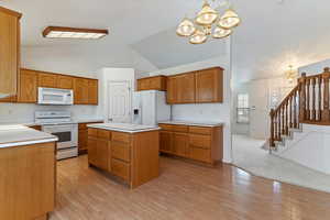 Kitchen with white appliances, suspended lighting, light countertops, vaulted ceiling, and a center island