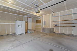 Garage with white fridge with ice dispenser, electric panel, and a garage door opener