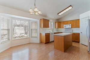 Kitchen with lofted ceiling, light countertops, a kitchen island, white appliances, and hanging lights
