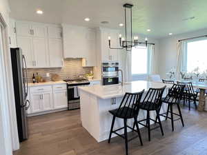 Kitchen with a center island with sink, white cabinetry, stainless steel appliances, and dark wood finished floors