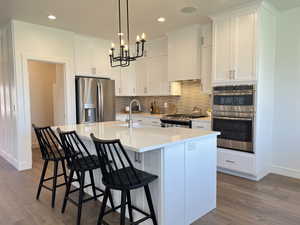 Kitchen with white cabinets, stainless steel appliances, a kitchen bar, tasteful backsplash, and dark wood finished floors