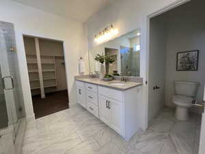 Bathroom featuring a shower stall, double vanity, a spacious closet, and light marble finish flooring