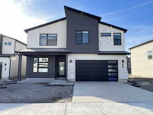 Contemporary home featuring a standing seam roof, stone siding, a garage, and concrete driveway
