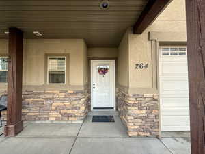 Doorway to property featuring a porch, stone siding, and stucco siding