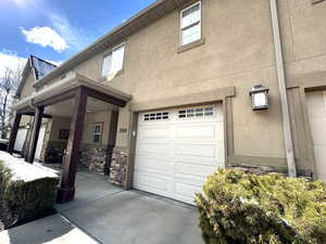 View of side of property featuring stone siding, a garage, stucco siding, and covered porch