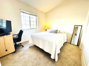 Bedroom with an office area, light carpet, and vaulted ceiling