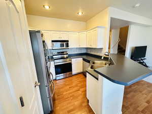 Kitchen with a peninsula, dark countertops, stainless steel appliances, and white cabinets