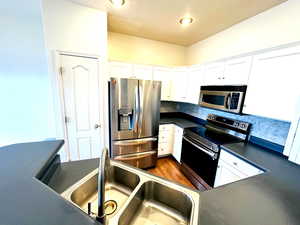 Kitchen featuring dark countertops, stainless steel appliances, white cabinetry, dark wood finished floors, and backsplash