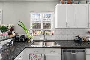 Kitchen featuring white cabinets, stainless steel dishwasher, and dark stone countertops