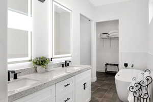 Full bath featuring double vanity, a freestanding tub, dark tile patterned flooring, and a spacious closet