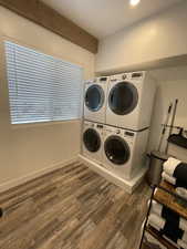 Laundry area featuring dark wood-type flooring, beam ceiling, stacked washer and dryer, and recessed lighting
