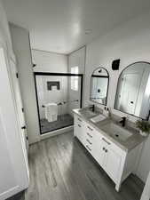 Full bathroom featuring double vanity, a stall shower, and wood finish floors