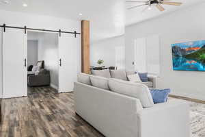Living area with a barn door, dark wood-type flooring, a ceiling fan, and recessed lighting