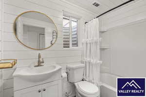 Full bathroom featuring wood walls, vanity, and shower / bathtub combination with curtain