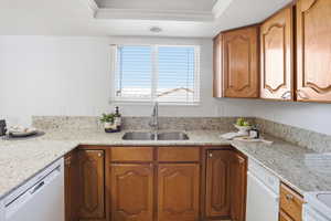 Kitchen with wood finish cabinets, light stone countertops, white appliances, ornamental molding, and a raised ceiling