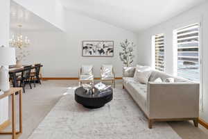 Living room with carpet flooring, a chandelier, and vaulted ceiling