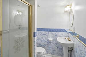 Full bath featuring a wainscoted wall, a shower stall, a textured ceiling, tile patterned flooring, and tile walls