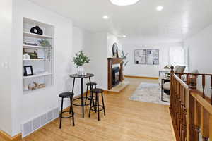 Sitting room featuring light wood finished floors, an upstairs landing, a glass covered fireplace, and recessed lighting