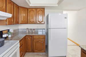 Kitchen with wood finish cabinets, light stone countertops, white appliances, and extractor fan