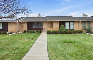 Single story home featuring a chimney, a front lawn, a shingled roof, brick siding, and covered porch